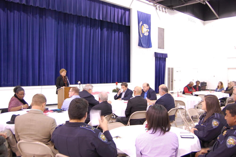 woman speaking at podium to audience of officers and others